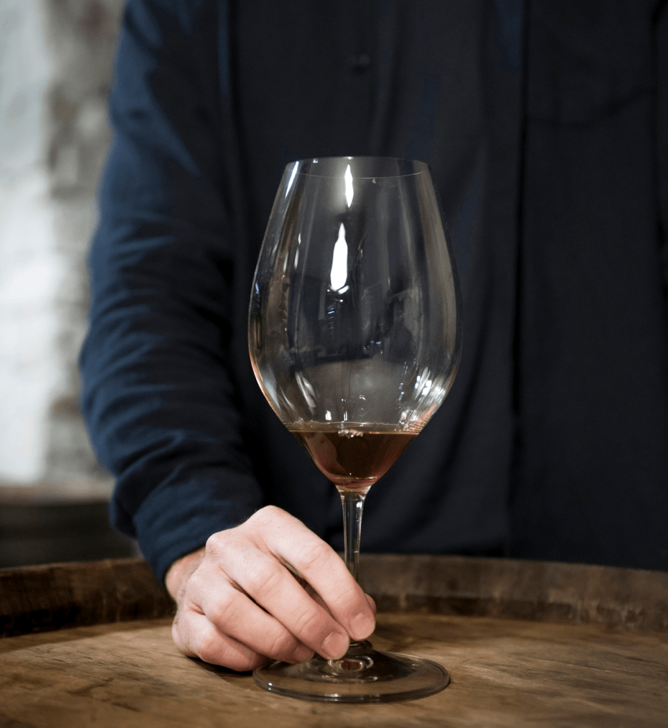Taça de vinho em avaliação sobre barril Experiência Vinícola Obstinado