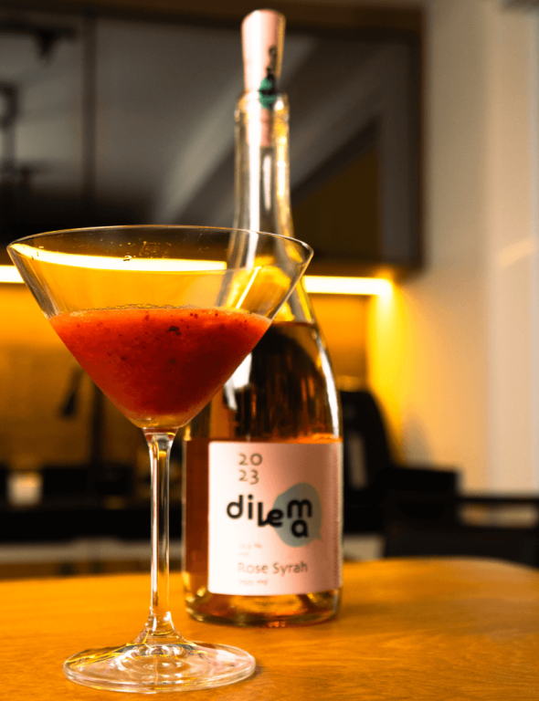 Taça de drink rosé ao lado de garrafa de vinho Dilema Experiência Vinícola Obstinado